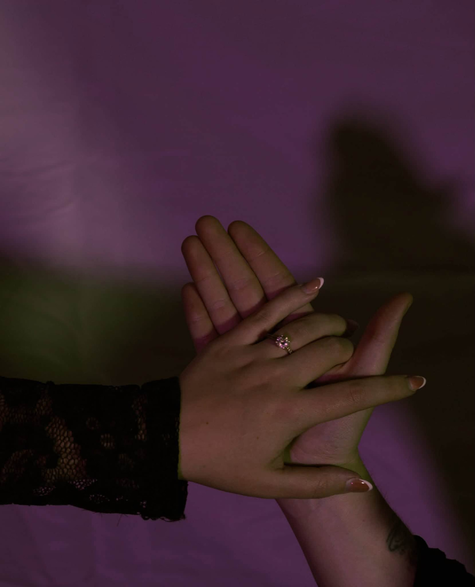 Engagement ring held between two hands in moody purple light